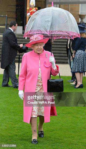 Queen Elizabeth II shelters from the rain under an umbrella during the first Royal Garden Party of the year in the grounds of Buckingham Palace on...