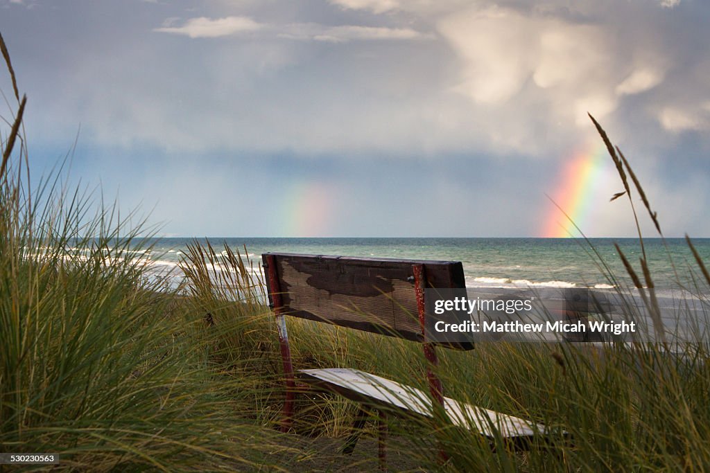 A bench overlooking the beach with rainbow