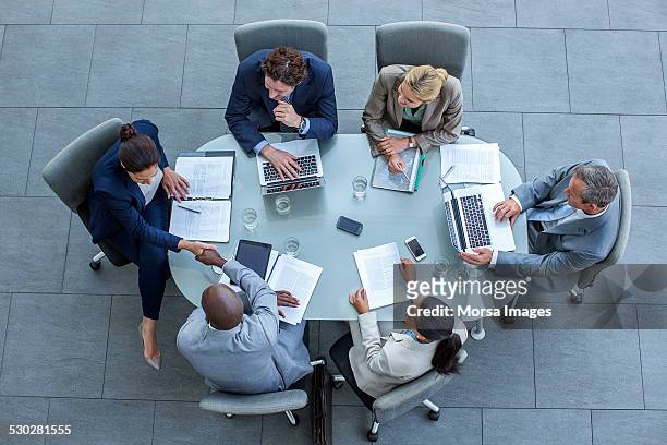 businesspeople shaking hands at conference table - board room stock-fotos und bilder