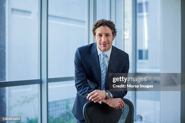 confident businessman leaning on chair - standing on chair stockfoto's en -beelden