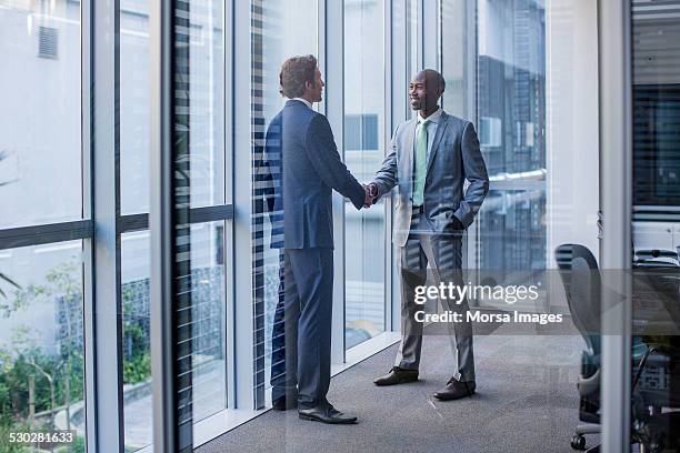 multi-ethnic businessmen shaking hands in office - handshake stock pictures, royalty-free photos & images