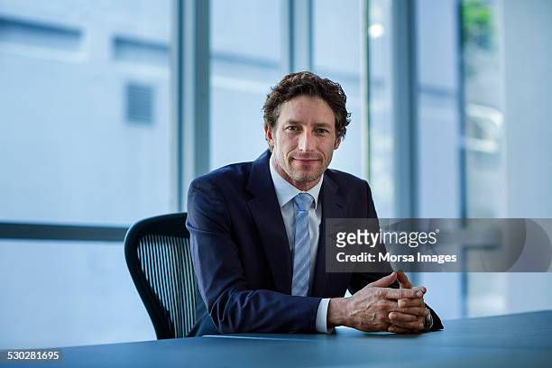 confident businessman sitting at conference table - mezzo busto foto e immagini stock