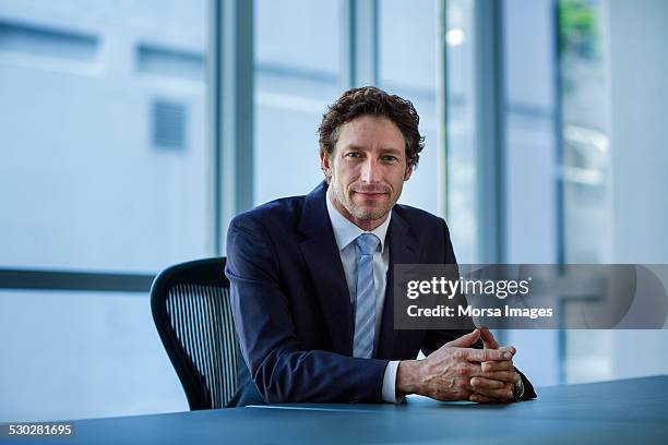 confident businessman sitting at conference table - traje completo - fotografias e filmes do acervo