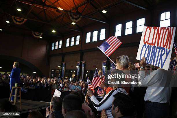 Attendees hold signs and wave American flags as Hillary Clinton, former Secretary of State and 2016 Democratic presidential candidate, left, speaks...