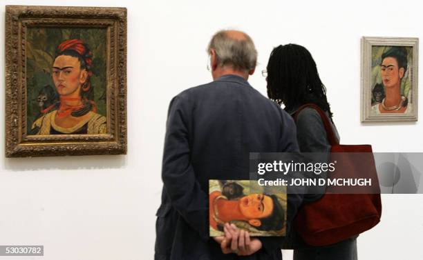 An couple carrying an exhibition guide stand between two paintings titled "Self Portrait with Monkey", part of the Frida Kahlo exhibition at the Tate...