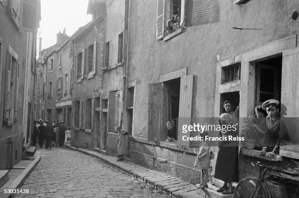 Local people watch as a group of British pilgrims passes through a French town on its way to the Benedictine abbey at Vezelay, August 1946. The...