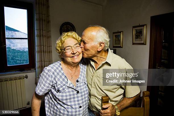 senior man kissing senior woman in cheek - travel loyalty stock pictures, royalty-free photos & images