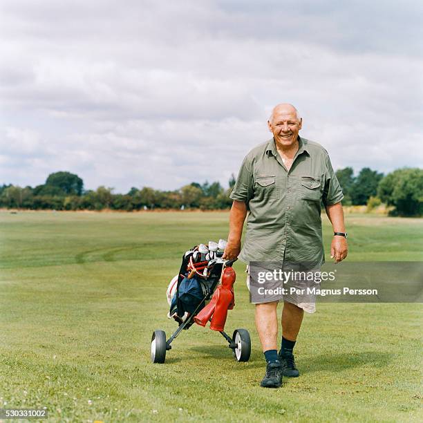 a golfer walks on a golf course - fat bald men stock pictures, royalty-free photos & images