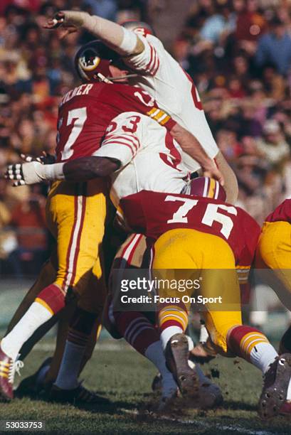 Washington Redskins' quarterback Billy Kilmer throws a pass but gets tackled by two San Francisco 49ers players.