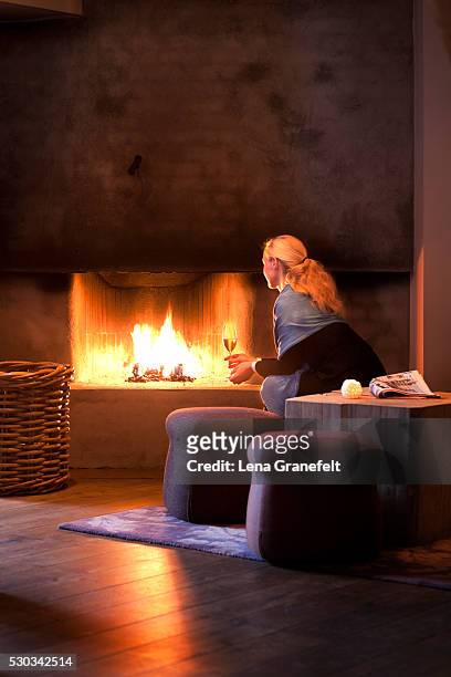 woman sitting with wineglass and looking at fireplace - unhappy woman blonde glasses stock pictures, royalty-free photos & images