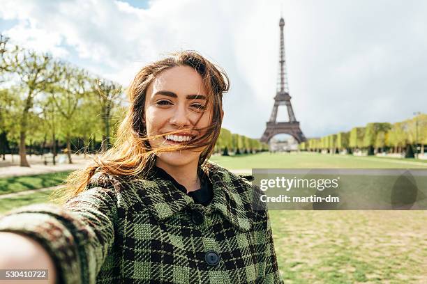 attractive woman taking selfie in front of the eiffel tower - woman eiffel tower stock pictures, royalty-free photos & images