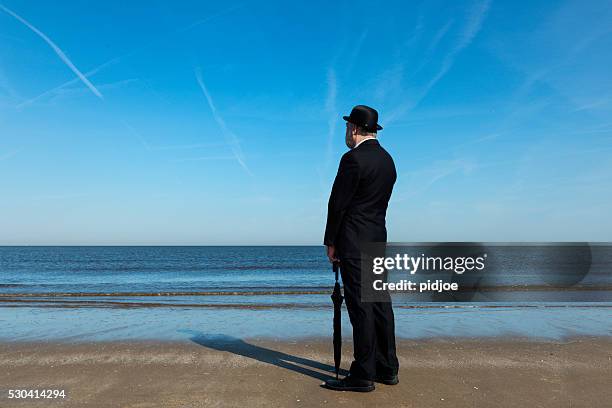 englishman standing on the beach, overlooking the sea - bowler hat stock pictures, royalty-free photos & images