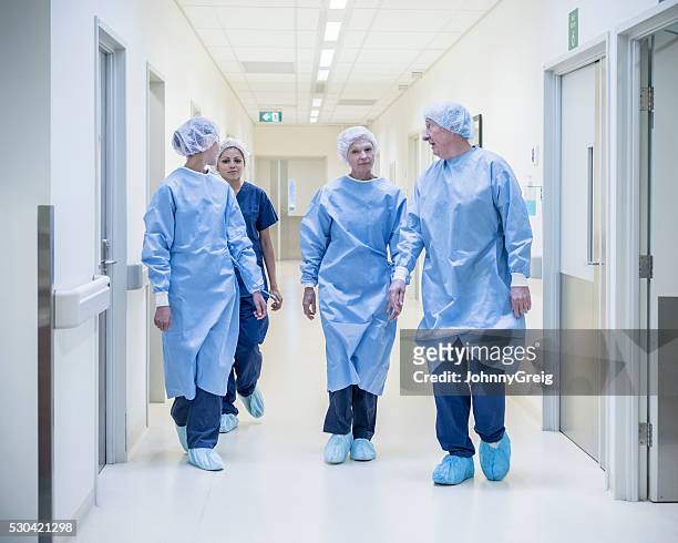 four surgeons in hospital corridor wearing scrubs, walking toward camera - surgeon walking stock pictures, royalty-free photos & images