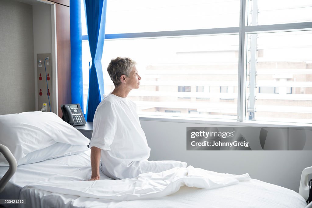 Senior woman sitting on hospital bed looking out of window
