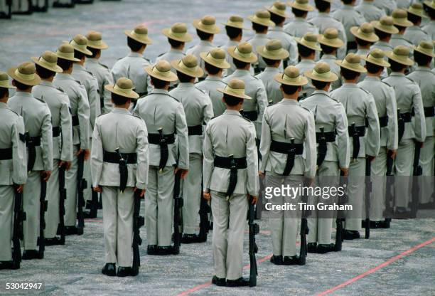 Ranks of Gurkha soldiers standing in lines with their traditional Kukri knives attached to scabbards on their belts and their rifles at their sides,...