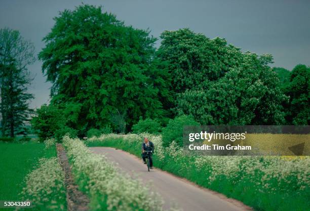 Man cycling along country lane near Coates in Gloucestershire, England.