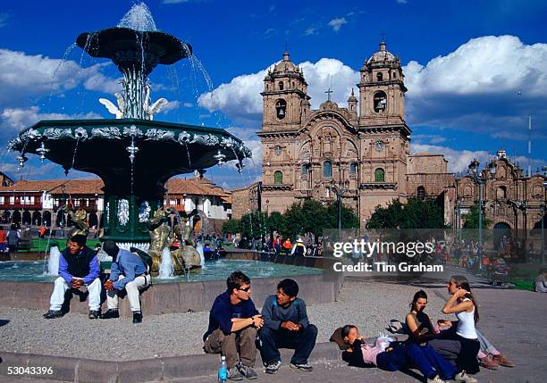 Young people gather in Plaza de Armas square by the fountain in Cuzco in front of La Compania church in the ancient capital of the Inca Empire, Peru,...