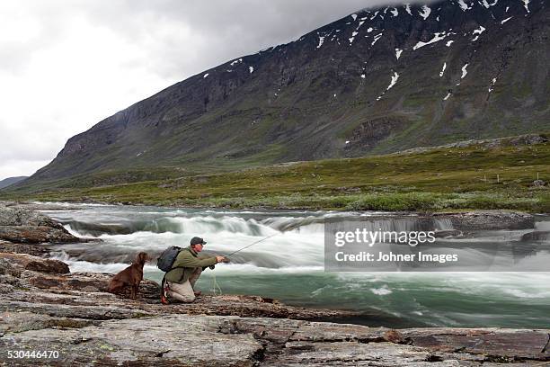 man fishing wit dog in river - fly fishing stockfoto's en -beelden