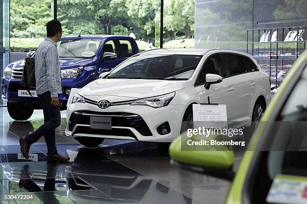 Man walks past a Toyota Motor Corp. Hilux vehicle, left, and Avensis vehicle displayed at the company's head office in Tokyo, Japan, on Wednesday,...