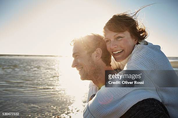 man carrying woman piggyback on the beach - mid adult stock-fotos und bilder