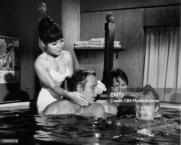 American actor Alan Alda laughs as Wayne Rogers makes a funny face while McLean Stevenson is bathed by a young woman as they all enjoy a soak in a...
