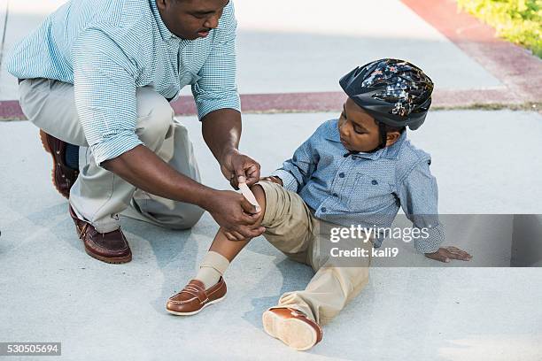 african american father putting bandage on son's knee - knees together 個照片及圖片檔