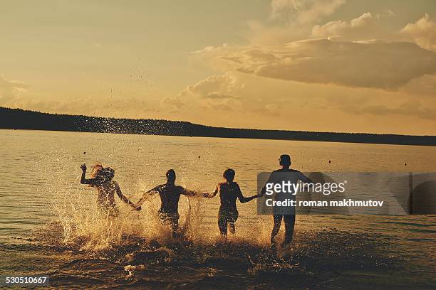 four people running in the evening waters - praia noite imagens e fotografias de stock