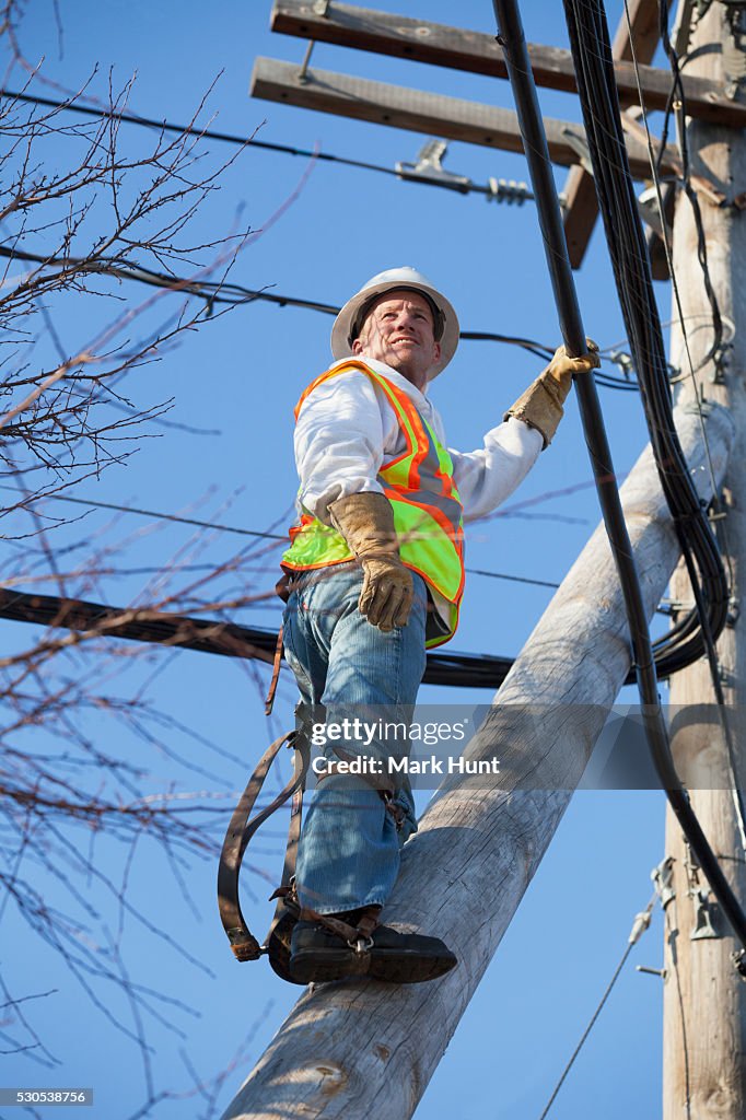 Cable lineman climbing a pole brace to cable bundles on power pole