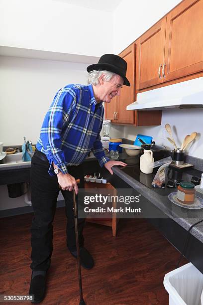 man with multiple sclerosis standing in his accessible kitchen with a cane - man fedora room stock pictures, royalty-free photos & images