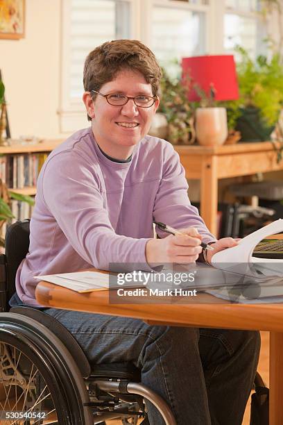 businesswoman with multiple sclerosis in a wheelchair doing paperwork at home - multiple sclerosis fotografías e imágenes de stock