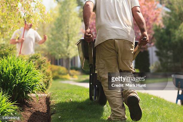 landscaper carrying mulch to a garden in wheelbarrow - landscape gardener foto e immagini stock