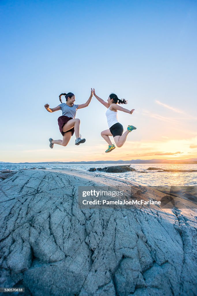 Two Girls Jumping and Giving High Fives on Rocky Beach