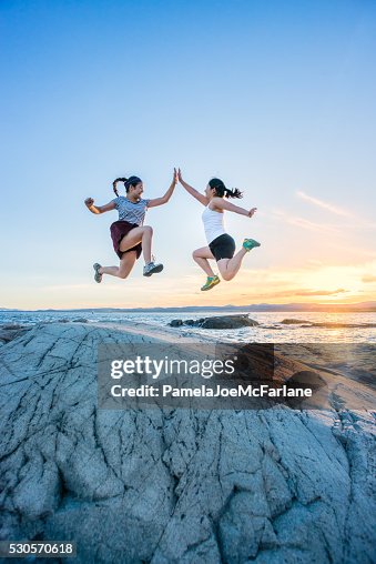 Two Girls Jumping and Giving High Fives on Rocky Beach Two Girls Jumping and Giving High Fives on Rocky Beach