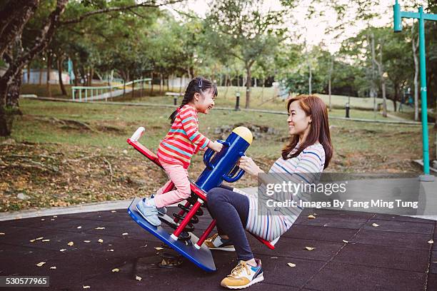 mom playing seesaw with daughter in playground - seesaw foto e immagini stock