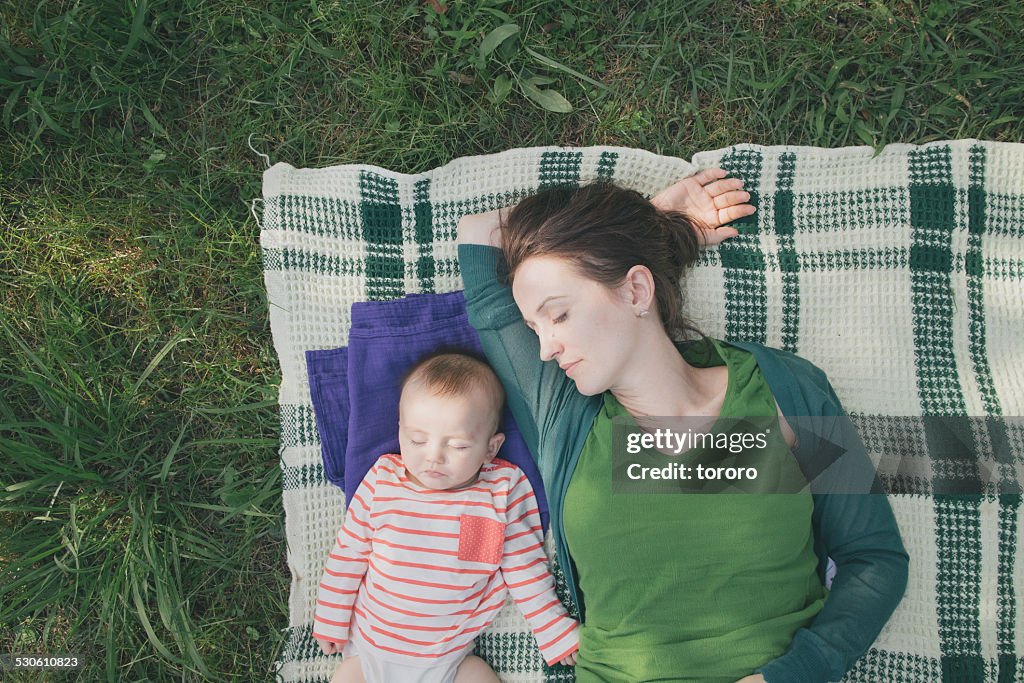 Mother and baby sleeping on blanket on grass