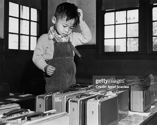 Young boy appears confused while searching for his lunchbox among a mass of matching lunchboxes at school.