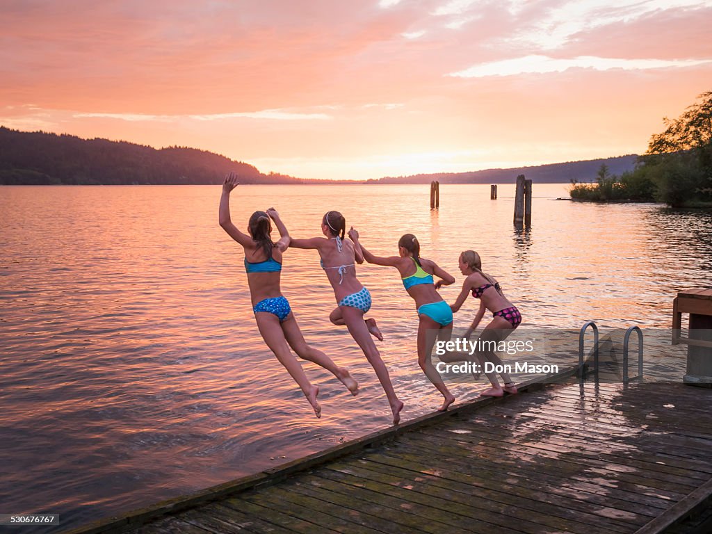 Girls jumping into lake from wooden dock