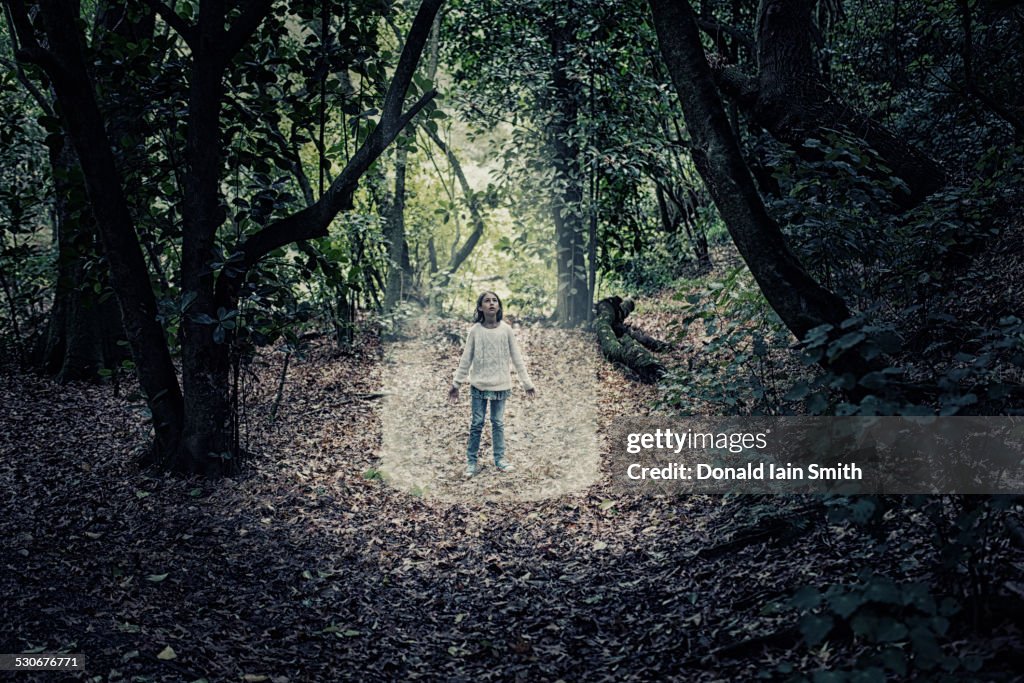 Mixed race girl standing in beam of light in forest