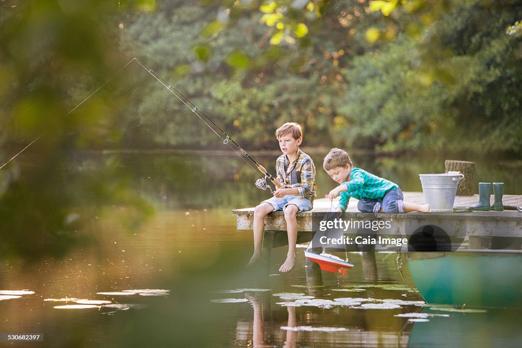 Boys fishing and playing with toy sailboat at lake