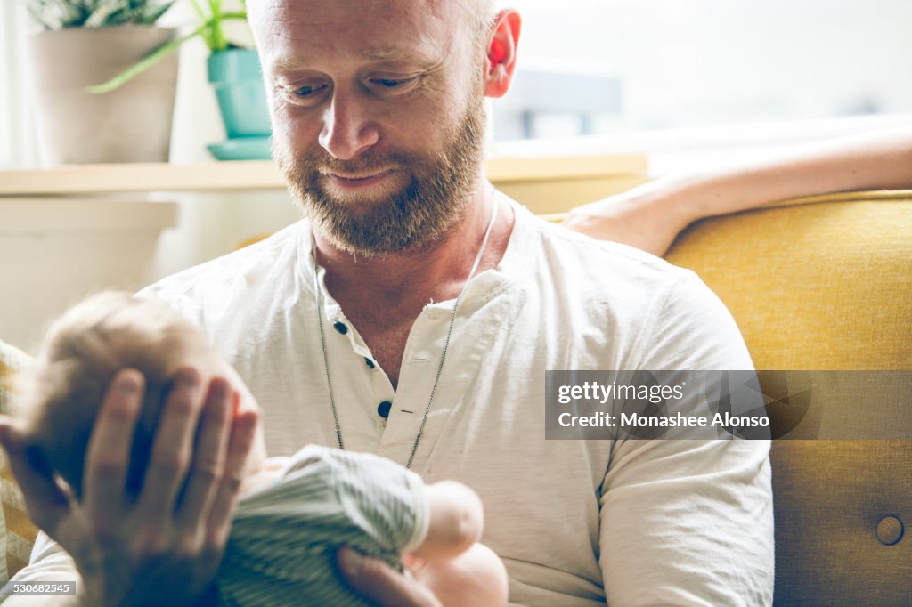 Porträt des Vaters, der das Baby hält und neben der Mutter auf dem Sofa sitzt