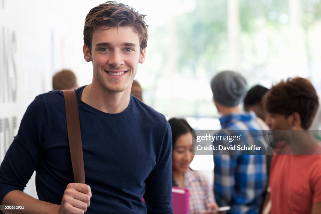 Portrait of smiling university student standing in corridor during break, people in background talking