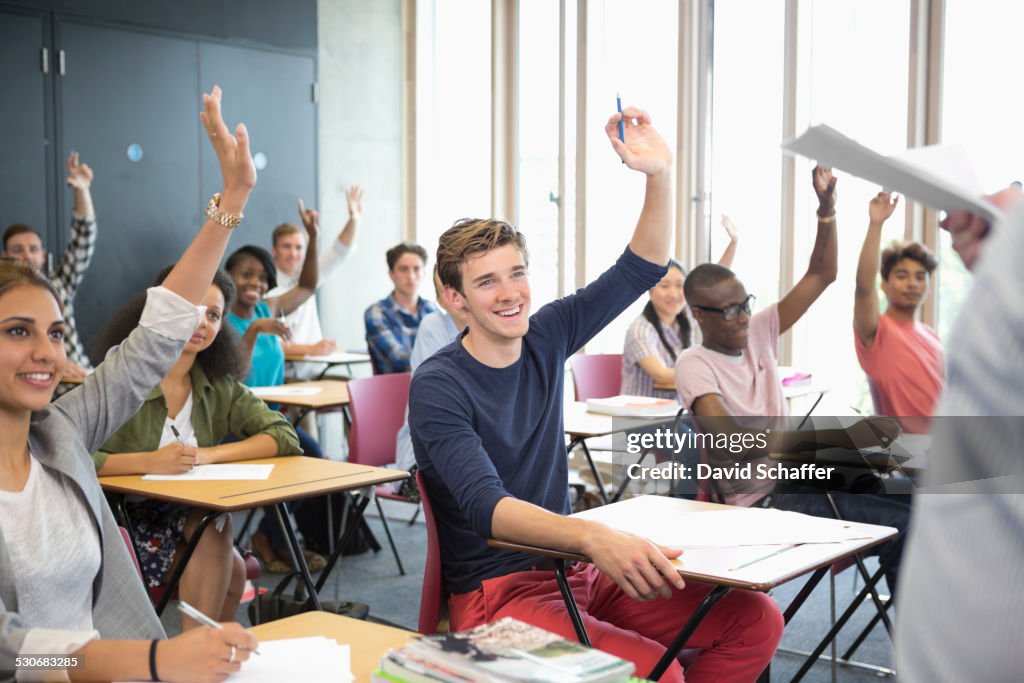 View of smiling students sitting at desks in classroom with arms raised