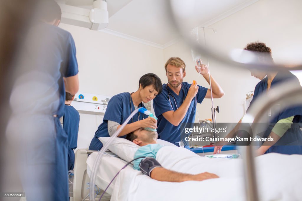 Doctor holding oxygen mask over patient, male doctor adjusting IV drip