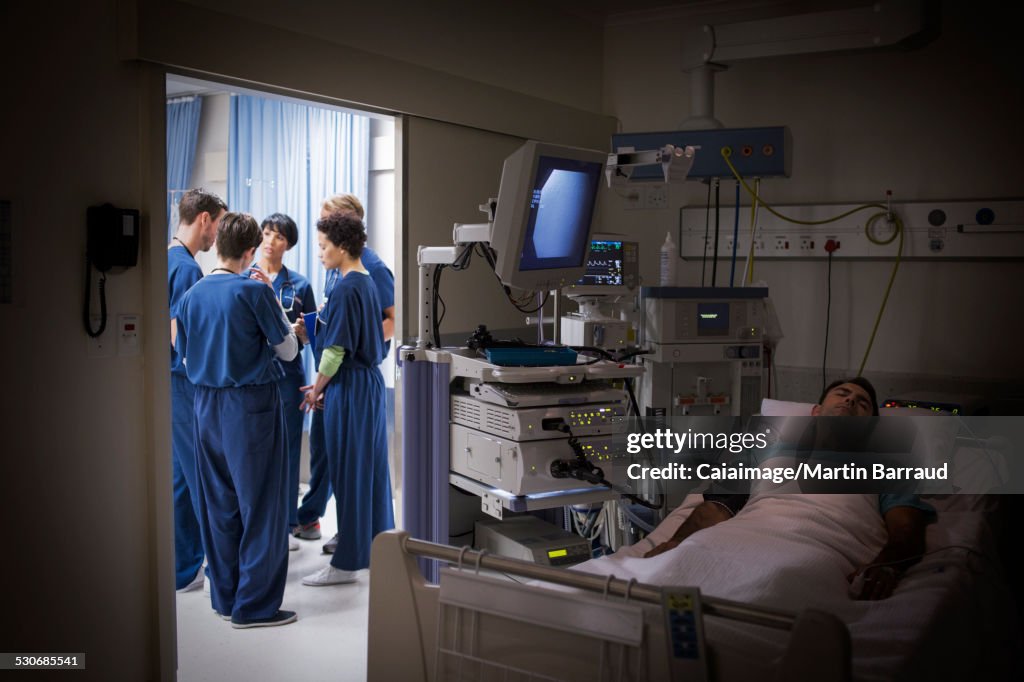 Patient lying in bed in intensive care unit, team of doctors discussing in background