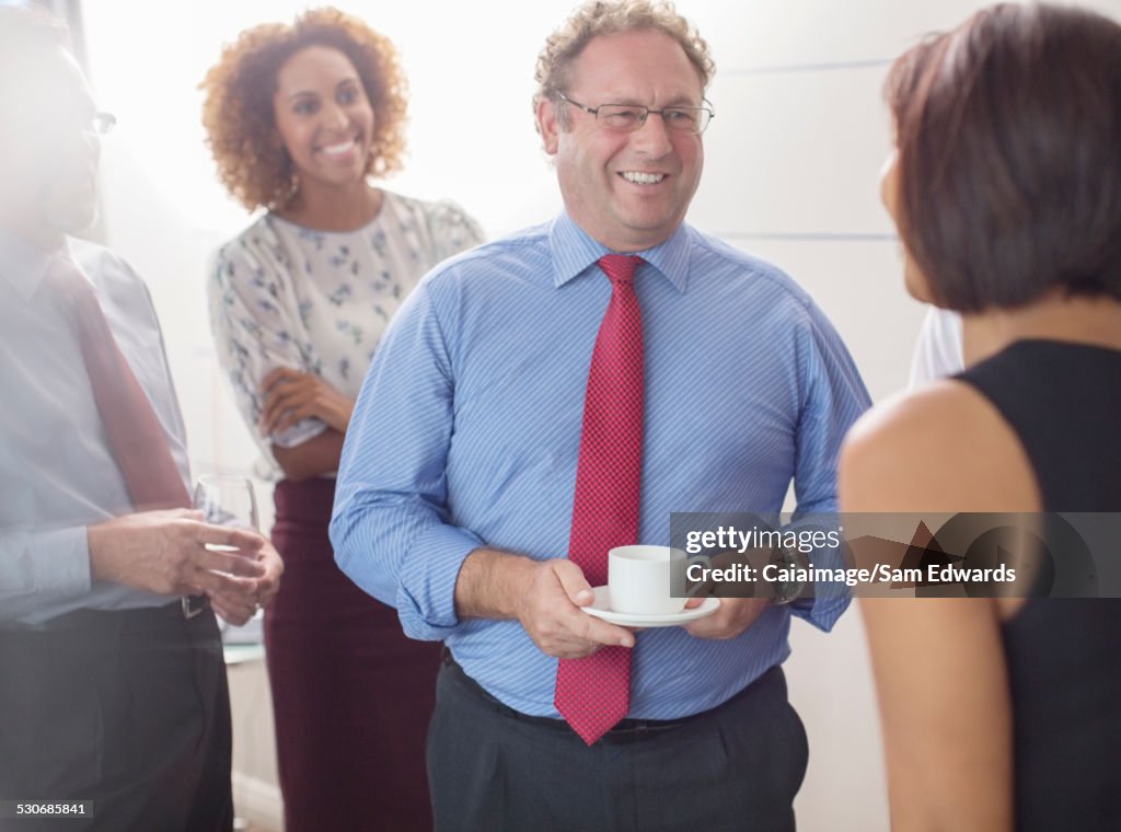 Businessman talking to colleagues in office and holding coffee cup