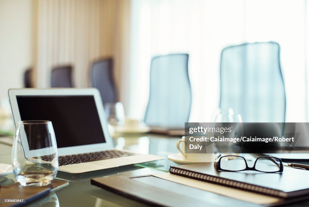 Laptop, eyeglasses and diary on conference table in empty conference room