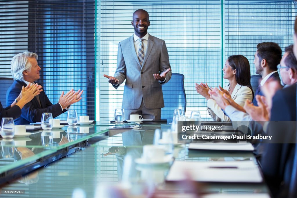 Businessman giving speech in conference room, colleagues clapping hands