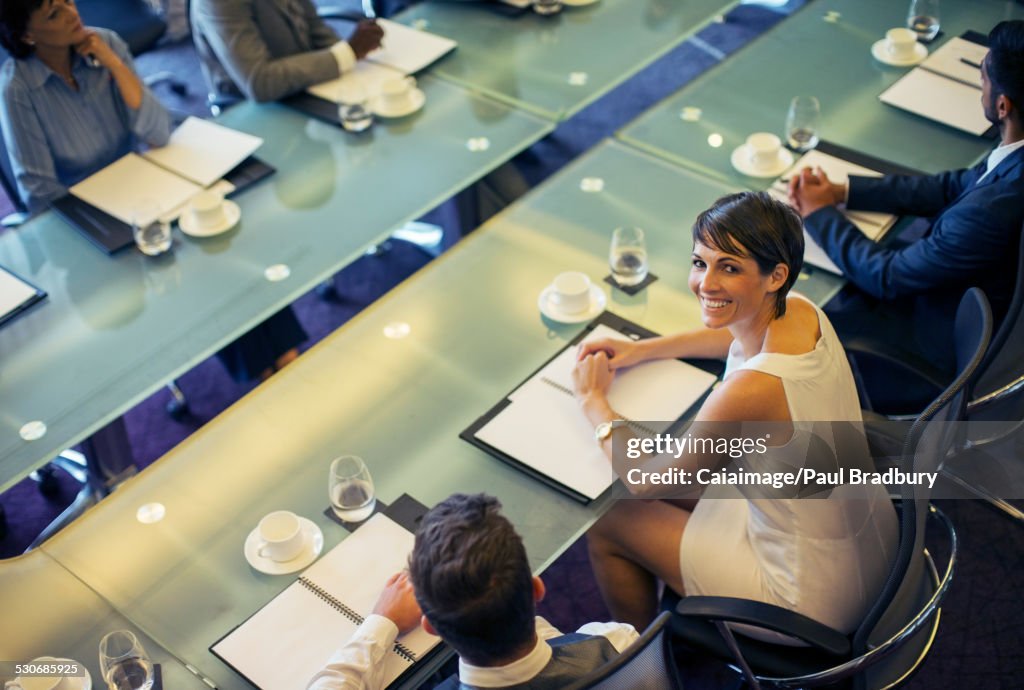 High angle view of smiling businesswoman looking at camera and sitting in conference room