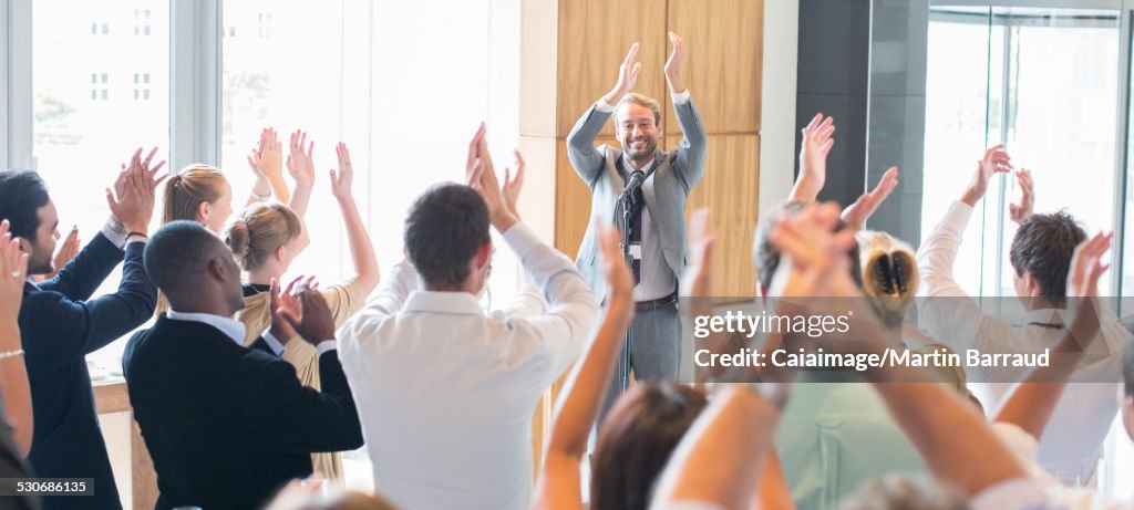 Ritratto di uomo sorridente in piedi davanti al pubblico nella sala conferenze, applaudendo