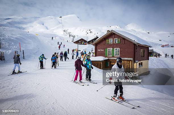 skiers in busy alpine ski resort beside chalets chairlift switzerland - grindelwald stock pictures, royalty-free photos & images